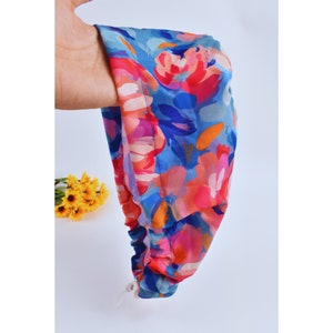 May include: A blue and pink floral print headband with a gathered elastic band. The headband is made of a soft, stretchy fabric and has a white drawstring closure.