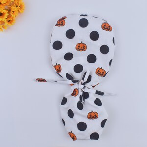 May include: White scrub hat with a black polka dot pattern and orange pumpkin faces.