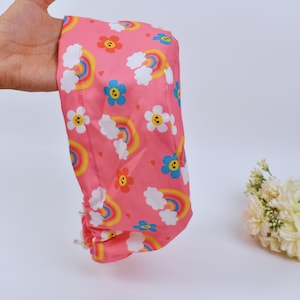 Puede incluir: Un gorro de quirófano rosa con un estampado de arcoíris y flores de colores.