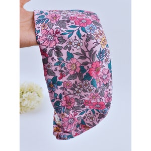 Op de afbeelding: Een roze hoofdband met een bloemenprint met roze, blauwe en groene bloemen op een lichtroze achtergrond.