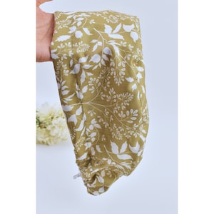 May include: A mustard yellow fabric scrunchie with a white floral pattern. The scrunchie is made of a soft, comfortable fabric and has a gathered elastic band.