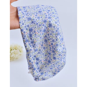 May include: A floral patterned scrub cap in a light blue and white color scheme. The cap features a repeating pattern of blue flowers, green leaves, and pink accents. The fabric is soft and appears to be cotton.