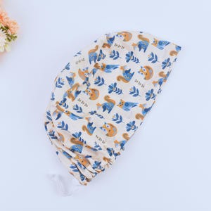 May include: A white fabric scrub cap with a pattern of blue and orange squirrels and leaves.