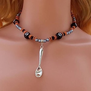 May include: A black and orange beaded choker necklace with silver beads and a silver spoon charm. The beads feature a black and white eight ball design.