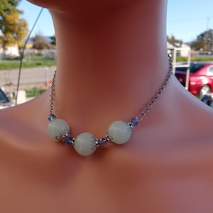 May include: A silver chain necklace with four white beads and small purple accents. The beads have a delicate, ornate design.