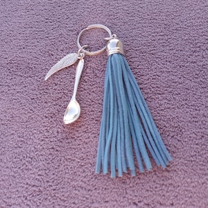 Op de afbeelding: Een zilveren sleutelhanger met een blauwe kwast, een kleine lepelhanger en een vleugelhanger.
