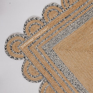 May include: A woven jute rug featuring a natural tan center and a scalloped edge border. The border is detailed with braided black and white fibers. The text SHEKHAWATIHANDICRAFT is printed in white across the upper left section of the rug.