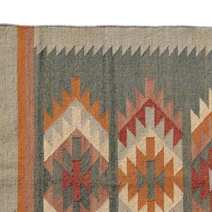 Puede incluir: Una alfombra con estampado geométrico y borde de flecos. La alfombra presenta una mezcla de colores marrón, naranja, rojo y gris.