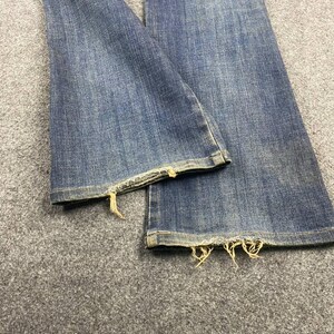 Puede incluir: Primer plano de vaqueros de mezclilla azules con dobladillos deshilachados. Los vaqueros tienen un dise&ntilde;o cl&aacute;sico de cinco bolsillos y un lavado medio. Los bordes deshilachados a&ntilde;aden un aspecto desgastado a los pantalones vaqueros.