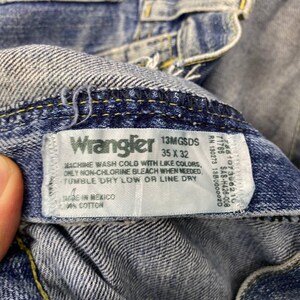 May include: Close-up of blue denim Wrangler jeans. The jeans have a label with the brand name, size 35 x 32, and care instructions. The jeans are made in Mexico and are 100% cotton.