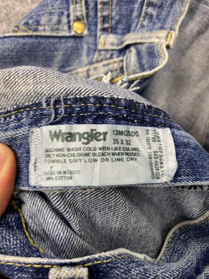May include: Close-up of blue denim Wrangler jeans. The jeans have a label with the brand name, size 35 x 32, and care instructions. The jeans are made in Mexico and are 100% cotton.