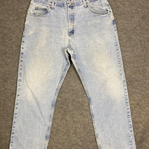 May include: Light blue denim jeans with a faded wash. The jeans have a classic five-pocket design, a button and zipper closure, and a straight leg. The hem of the jeans is slightly frayed.