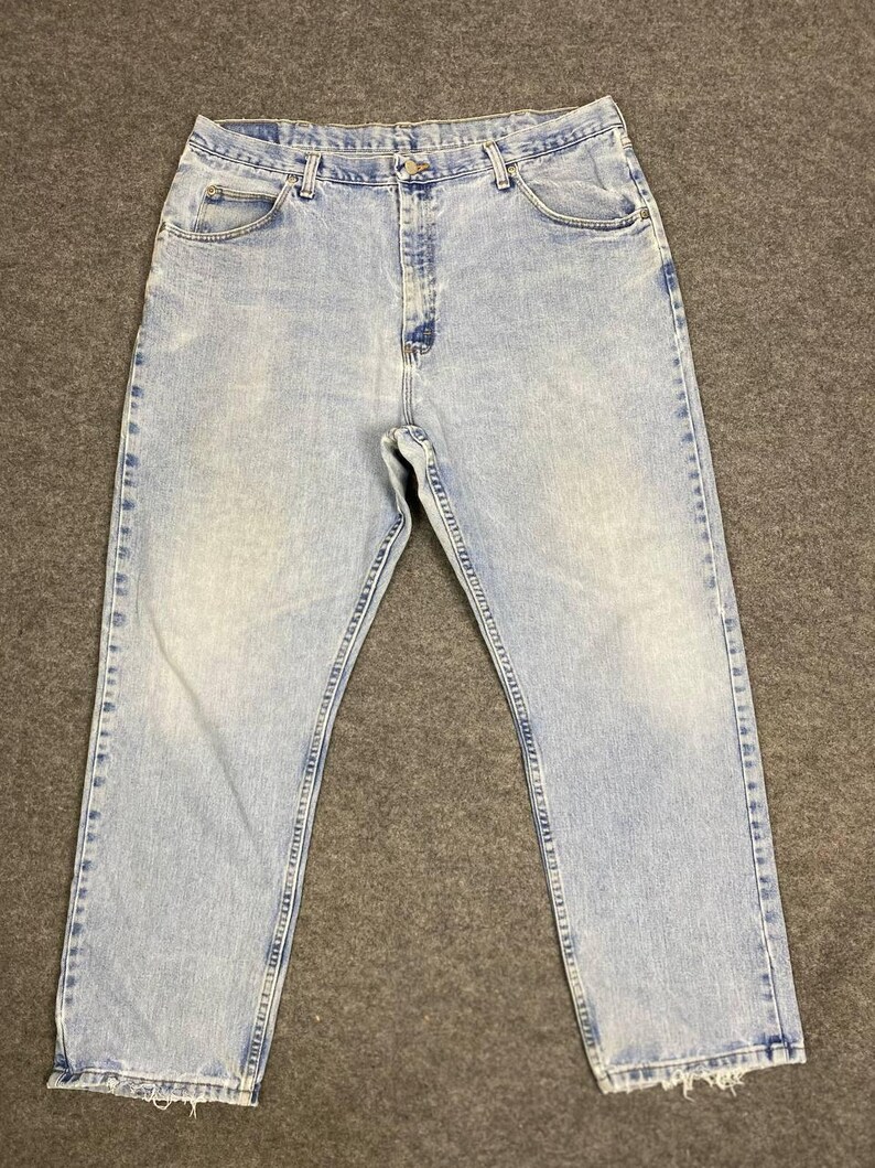 May include: Light blue denim jeans with a faded wash. The jeans have a classic five-pocket design, a button and zipper closure, and a straight leg. The hem of the jeans is slightly frayed.