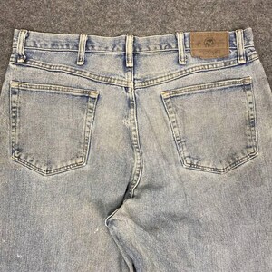 K&ouml;nnte beinhalten: Hellblaue Jeans mit klassischem F&uuml;nf-Taschen-Design. Die Jeans haben einen braunen Lederaufn&auml;her mit dem "Wrangler"-Logo auf der R&uuml;ckseite. Die Jeans haben ein verwaschenes Aussehen.