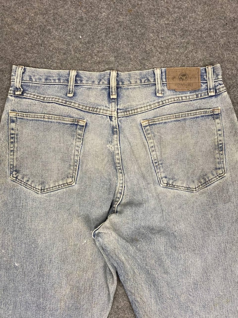 K&ouml;nnte beinhalten: Hellblaue Jeans mit klassischem F&uuml;nf-Taschen-Design. Die Jeans haben einen braunen Lederaufn&auml;her mit dem "Wrangler"-Logo auf der R&uuml;ckseite. Die Jeans haben ein verwaschenes Aussehen.