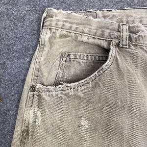 May include: Close-up of light gray denim jeans with distressed details. The jeans feature a classic five-pocket design, with visible wear and tear around the pockets and seams. The fabric has a faded appearance, suggesting a worn-in look.