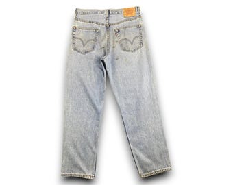 May include: Light blue denim jeans with a faded wash. The jeans have a classic five-pocket design, belt loops, and a leather patch on the back. The back pockets feature the iconic Levi's stitching.