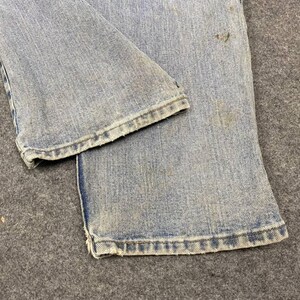 K&ouml;nnte beinhalten: Nahaufnahme einer hellblauen Jeans. Die Jeans weist Gebrauchsspuren auf, mit sichtbaren Flecken und Ausfransungen am Saum. Der Stoff hat ein verwaschenes Aussehen, was auf Alter oder Waschen hindeutet. Das Bild hebt die Textur und Details des Jeansstoffs hervor.
