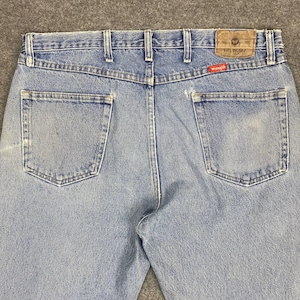 May include: Light blue denim jeans with two back pockets and a brown leather patch. The jeans feature the Wrangler logo on the patch and a red tag. The jeans have belt loops and a classic five-pocket design.