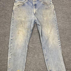 K&ouml;nnte beinhalten: Hellblaue Jeans aus Denim mit verblichener Waschung und sichtbaren Gebrauchsspuren. Die Jeans haben ein klassisches F&uuml;nf-Taschen-Design, einen Knopf- und Rei&szlig;verschluss sowie G&uuml;rtelschlaufen. Auf der Vorderseite der Jeans befinden sich Flecken und Verf&auml;rbungen.