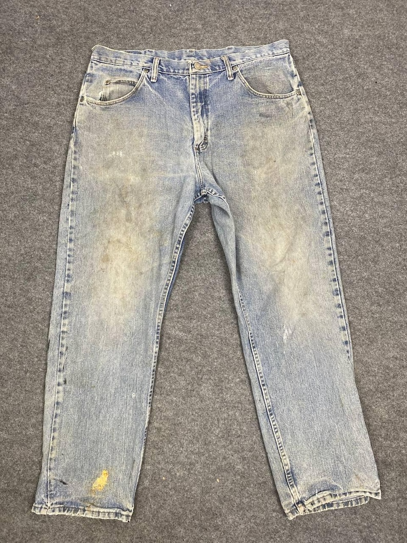 K&ouml;nnte beinhalten: Hellblaue Jeans aus Denim mit verblichener Waschung und sichtbaren Gebrauchsspuren. Die Jeans haben ein klassisches F&uuml;nf-Taschen-Design, einen Knopf- und Rei&szlig;verschluss sowie G&uuml;rtelschlaufen. Auf der Vorderseite der Jeans befinden sich Flecken und Verf&auml;rbungen.