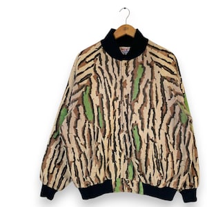 Può includere: Giacca bomber vintage con un motivo unico. La giacca presenta una base color crema con disegni a righe verticali marroni, nere e verdi. Ha colletto, polsini e fascia in vita neri. La giacca è appesa a una gruccia di legno.