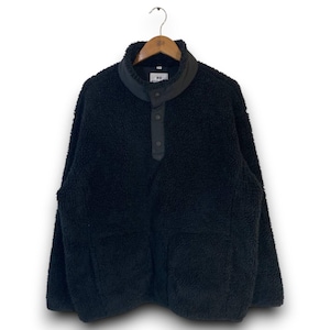 Könnte beinhalten: Ein schwarzer Fleece-Pullover mit hohem Kragen und Knopfverschluss. Das langärmlige Kleidungsstück hat zwei Vordertaschen und hängt an einem Holzbügel. Das Fleece-Material wirkt weich und strukturiert.
