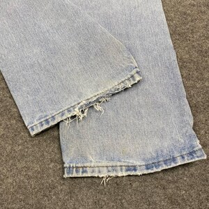 May include: Close-up of light blue denim jeans. The bottom hems are frayed and distressed, with visible threads. The jeans show signs of wear and tear, with slight discoloration.