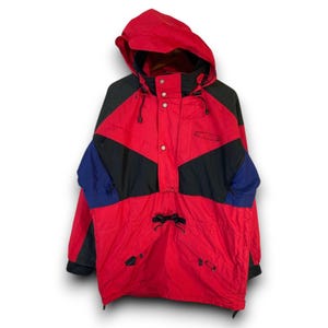 May include: A red, black, and blue hooded anorak jacket. The jacket features a color block design with a red body, black center panel, and blue accents on the sleeves. It has a drawstring at the waist and a front pocket.