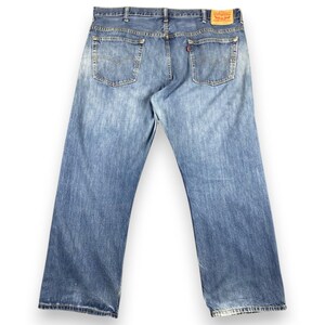 May include: Light blue denim jeans with a faded wash. The jeans have a classic five-pocket design, a button and zipper closure, and a red Levi's tag on the back. The jeans are a relaxed fit.