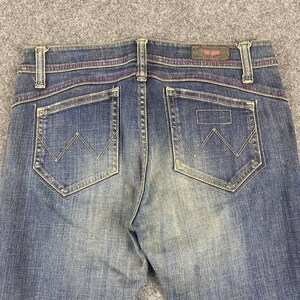 Puede incluir: Primer plano de la parte trasera de unos vaqueros azules. Los vaqueros tienen dos bolsillos traseros con un dise&ntilde;o de 'W' cosido. Las costuras son de color rosa en contraste. Una peque&ntilde;a etiqueta de cuero es visible en la cintura.