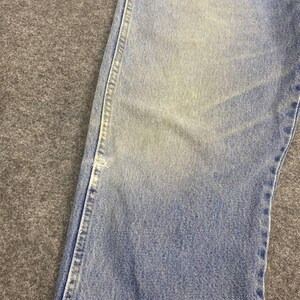 May include: Close-up of light blue denim jeans. The jeans show signs of wear with faded areas and visible stitching along the seams. The fabric has a slightly distressed appearance, suggesting a vintage or well-worn style.