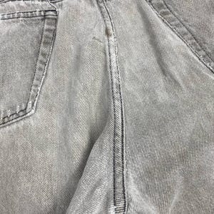 May include: Close-up of light gray denim jeans. The jeans have visible stitching in black thread along the seams and pockets. The fabric has a textured appearance with vertical lines.