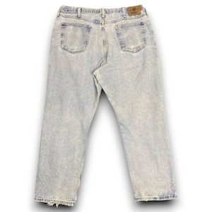 May include: Light wash denim jeans with a faded appearance. The jeans have a classic five-pocket design, a button and zipper closure, and a leather patch on the back. The jeans have a straight leg and a slightly distressed hem.