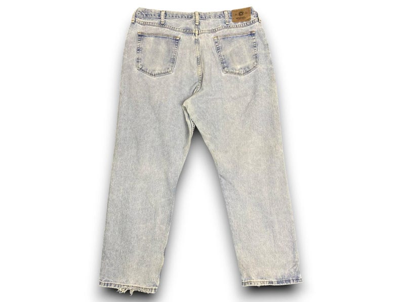 May include: Light wash denim jeans with a faded appearance. The jeans have a classic five-pocket design, a button and zipper closure, and a leather patch on the back. The jeans have a straight leg and a slightly distressed hem.