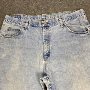 May include: Light blue denim jeans with a button closure and classic five-pocket design. The jeans have a faded wash and are made of durable denim material. The image shows the upper portion of the jeans, including the waistband and pockets.
