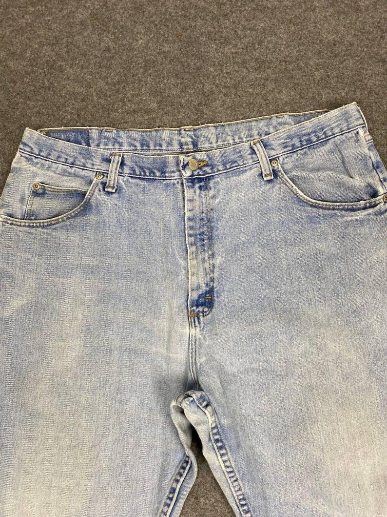 May include: Light blue denim jeans with a button closure and classic five-pocket design. The jeans have a faded wash and are made of durable denim material. The image shows the upper portion of the jeans, including the waistband and pockets.