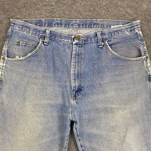 May include: Light blue denim jeans with a classic five-pocket design. The jeans have a button and zipper closure, belt loops, and a faded wash for a vintage look. The jeans are made of durable denim.