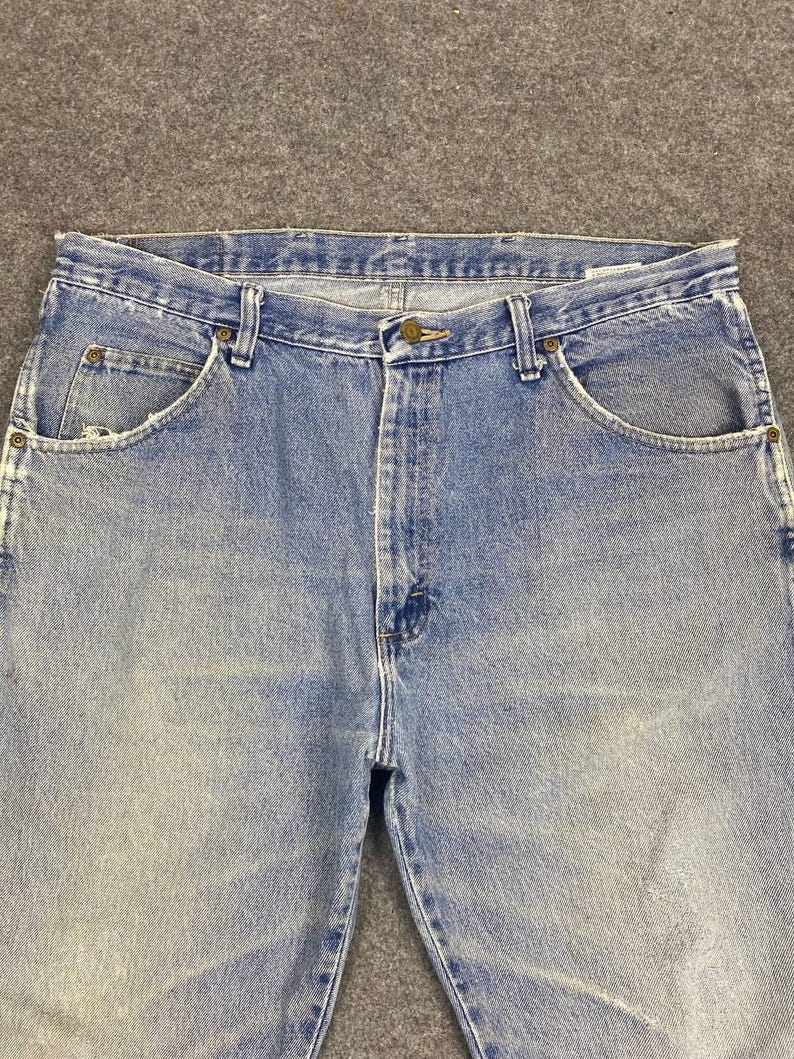 May include: Light blue denim jeans with a classic five-pocket design. The jeans have a button and zipper closure, belt loops, and a faded wash for a vintage look. The jeans are made of durable denim.