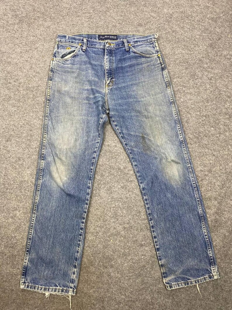 May include: Faded blue denim jeans with a classic five-pocket design. The jeans show signs of wear and fading, with a straight leg cut. The stitching is visible along the seams and pockets. The jeans are laid flat on a gray surface.