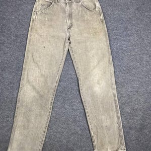 May include: Faded olive green denim jeans with a classic five-pocket design. The jeans have a straight leg cut and distressed, frayed hems. The fabric shows signs of wear and tear.