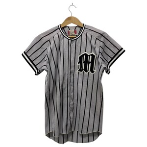 Puede incluir: Camiseta de béisbol a rayas grises y blancas con rayas verticales negras. La camiseta tiene mangas cortas con ribetes negros y blancos y un gran parche negro con la letra "M" en el pecho. Es abotonada y cuelga de una percha de madera.