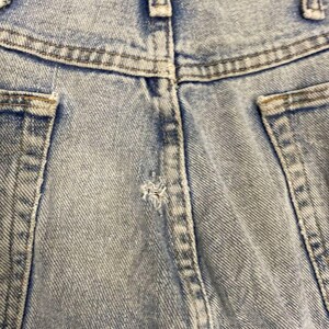 K&ouml;nnte beinhalten: Nahaufnahme der R&uuml;ckseite einer hellblauen Jeans. Das Bild zeigt den Bund, die G&uuml;rtelschlaufen und die Taschen. Der Denim hat ein verwaschenes, abgenutztes Aussehen mit einem kleinen Riss in der N&auml;he der Mittelnaht.