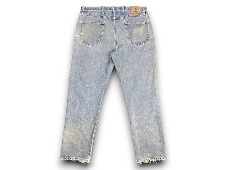 May include: Light blue denim jeans with a faded wash and distressed details. The jeans have a classic five-pocket design, a button and zipper closure, and a leather patch on the back. The jeans are a vintage style.