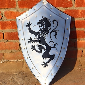 May include: A silver shield with a black lion rampant design. The shield is decorated with metal rivets around the edge.