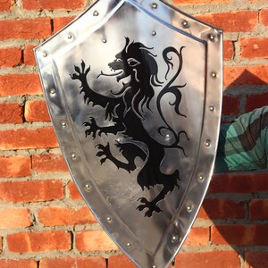 May include: A silver shield with a black lion design. The shield has a pointed bottom and is decorated with metal rivets around the edge.