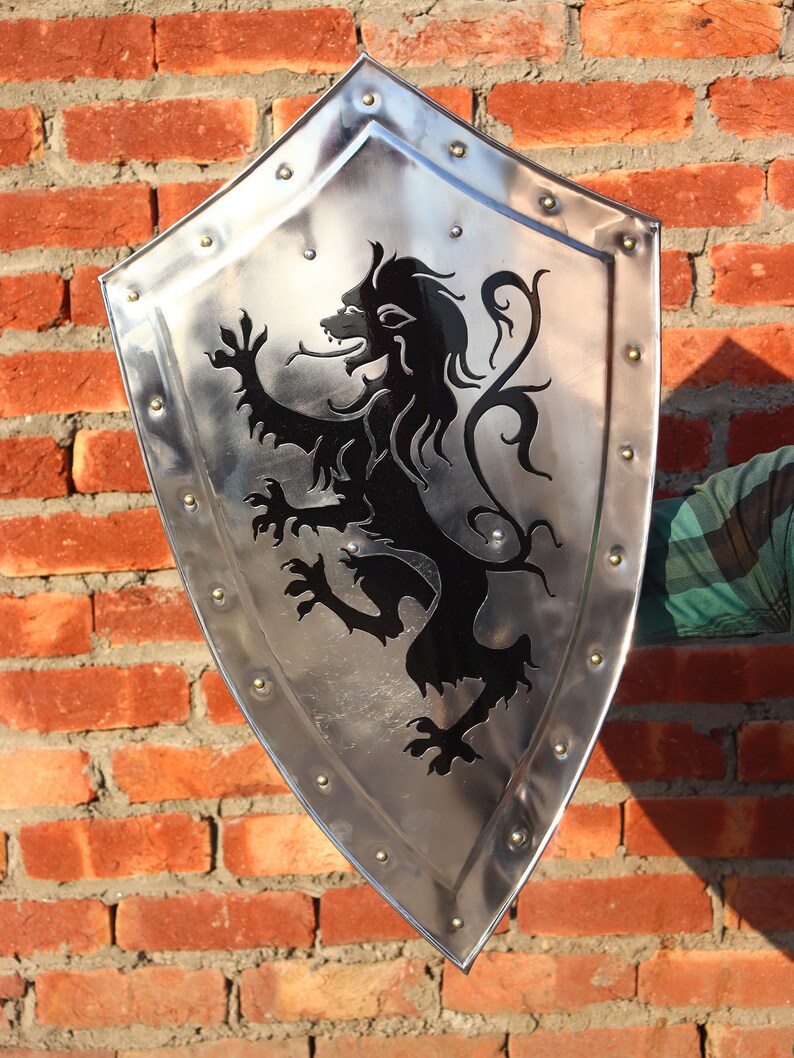 May include: A silver shield with a black lion design. The shield has a pointed bottom and is decorated with metal rivets around the edge.