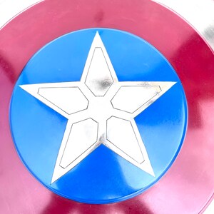 Pu&ograve; includere: Uno scudo di Capitan America rosso, bianco e blu con una stella argentata a cinque punte al centro.