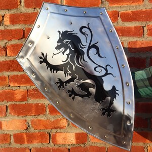 May include: A silver shield with a black lion design. The shield has a pointed bottom and is decorated with rivets around the edge.