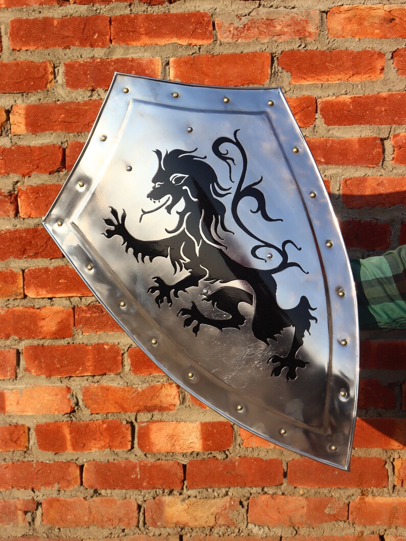 May include: A silver shield with a black lion design. The shield has a pointed bottom and is decorated with rivets around the edge.